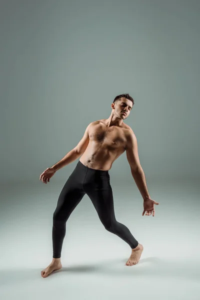 Guapo bailarín con los ojos cerrados en leggings negros bailando contemporáneo sobre fondo oscuro - foto de stock