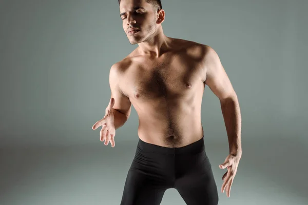 Guapo bailarín con los ojos cerrados en leggings negros bailando contemporáneo sobre fondo gris - foto de stock