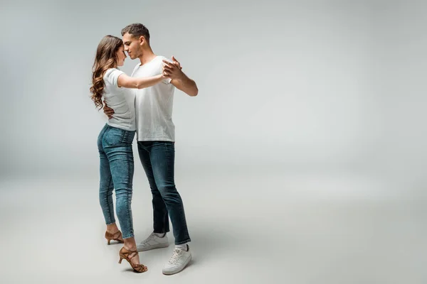 Bailarines sonrientes en camisetas y jeans bailando bachata sobre fondo gris - foto de stock