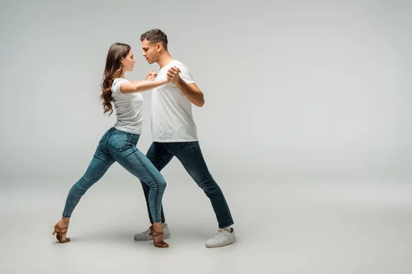 Side view of dancers in t-shirts and jeans dancing bachata on grey background — Stock Photo