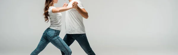 Panoramic shot of dancers in t-shirts and jeans dancing bachata isolated on grey — Stock Photo