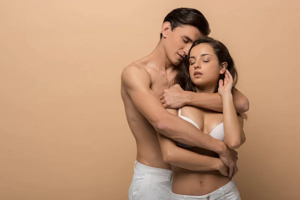 Shirtless boyfriend hugging beautiful girlfriend in white bra, isolated on beige — Stock Photo