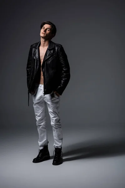 Bellissimo uomo sexy in jeans bianchi e giacca di pelle nera, su grigio — Foto stock