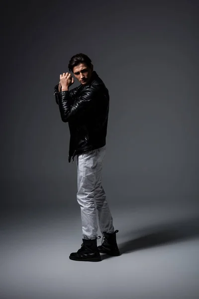 Giovane uomo in jeans bianchi e giacca di pelle nera, su grigio — Foto stock
