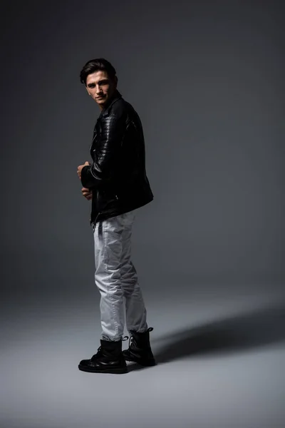 Handsome man in white jeans and black leather jacket, on grey — Stock Photo