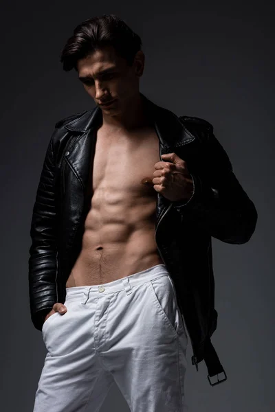Сексуальный мужчина без рубашки в белых джинсах и черной кожаной куртке, изолированный на сером — стоковое фото