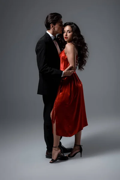 Romantic young couple in suit and red silk dress hugging on grey — Stock Photo