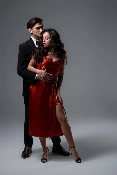 Couple sensuel en costume et robe de soie rouge étreignant sur gris — Photo de stock