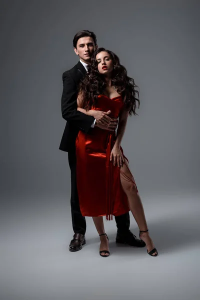 Romantic couple in suit and red silk dress hugging on grey — Stock Photo