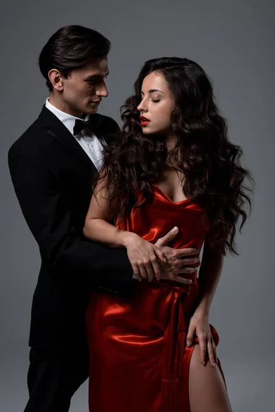 Young couple in suit and red silk dress hugging isolated on grey — Stock Photo