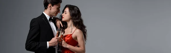 Panoramic shot of Romantic couple holding champagne glasses and looking at each other, isolated on grey — Stock Photo