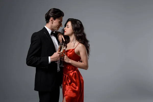 Casal segurando copos de champanhe enquanto olham um para o outro, isolados em cinza — Fotografia de Stock