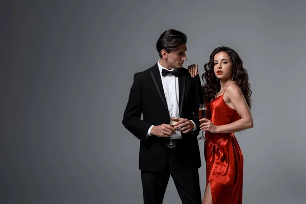 Beautiful festive couple holding champagne glasses, isolated on grey — Stock Photo