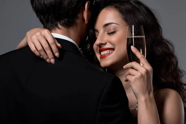 Happy smiling woman hugging man while holding glass of champagne, isolated on grey — Stock Photo