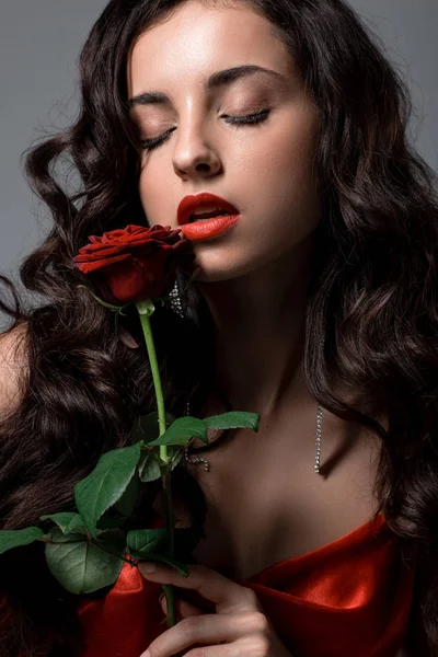 Seductive woman in red silk dress holding rose flower, isolated on grey — Stock Photo