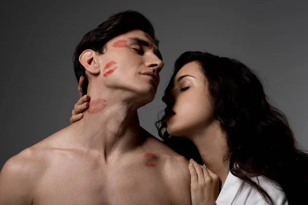 Femme passionnée embrassant homme avec des empreintes rouges à lèvres, isolé sur gris — Photo de stock