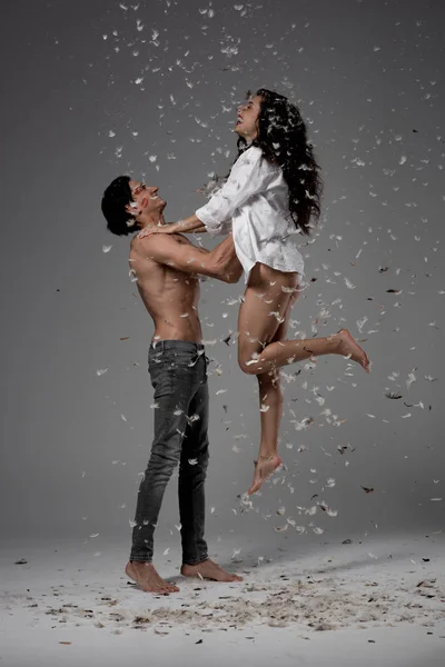 Cheerful couple jumping and having fun on grey with feathers — Stock Photo