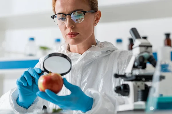 Selective focus of biologist looking at apple with magnifying glass — Stock Photo