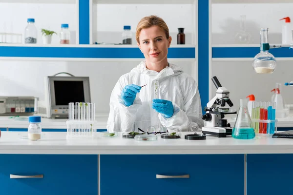 Biólogo sonriente sosteniendo el tubo de ensayo y mirando la cámara en el laboratorio - foto de stock