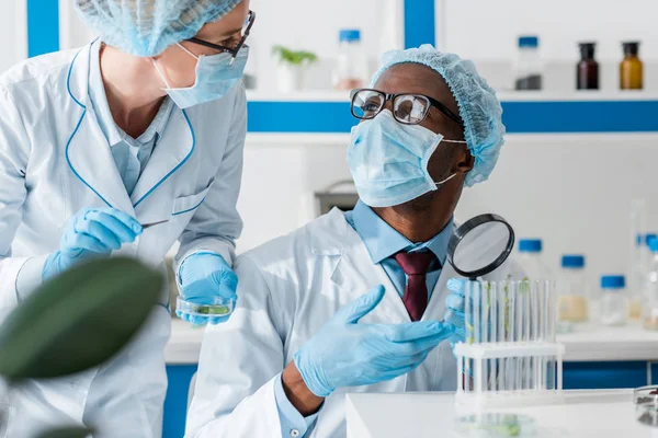 Biologiste afro-américain en masque médical parlant avec un collègue en laboratoire — Photo de stock
