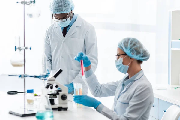 Biólogos multiculturales en batas blancas haciendo pruebas en laboratorio - foto de stock