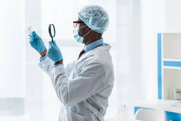 Vue latérale du biologiste afro-américain regardant les feuilles avec loupe — Photo de stock