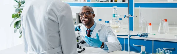 Colpo panoramico del biologo afro-americano sorridente che guarda il suo collega — Foto stock