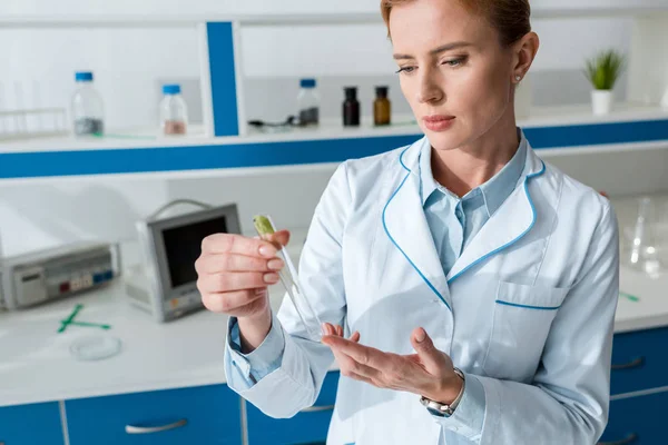 Biologe im weißen Kittel hält Reagenzglas mit Blättern — Stockfoto