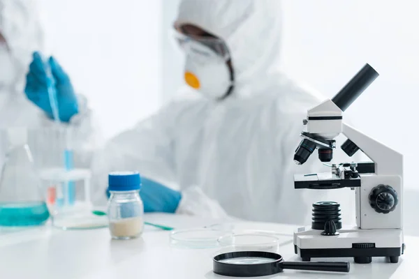 Selective focus of microscope and magnifying glass on table and african american scientist working in lab — Stock Photo