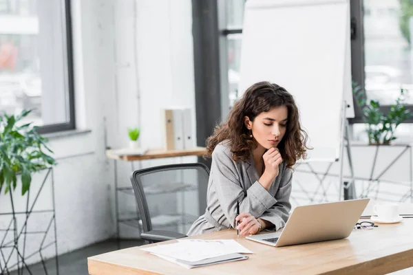 Pensive account manager sat at the table and looking to laptop — стоковое фото