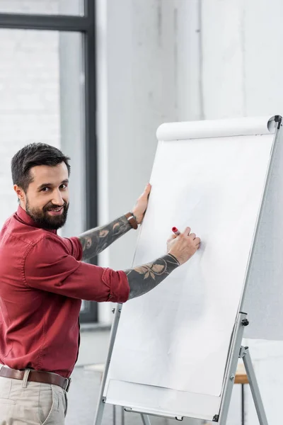 Handsome and smiling account manager standing near flipchart and looking at camera — Stock Photo