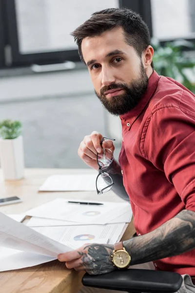 Bello account manager seduto a tavola e tenere gli occhiali — Foto stock