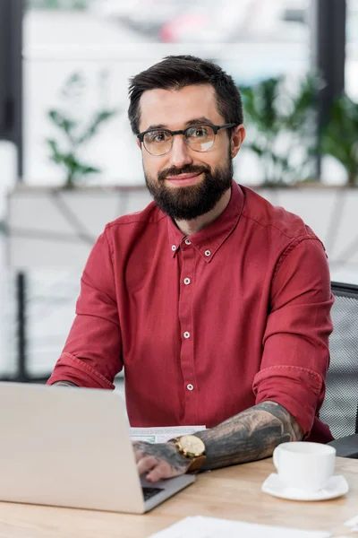 Gutaussehender und lächelnder Account Manager, der am Tisch sitzt und in die Kamera schaut — Stockfoto