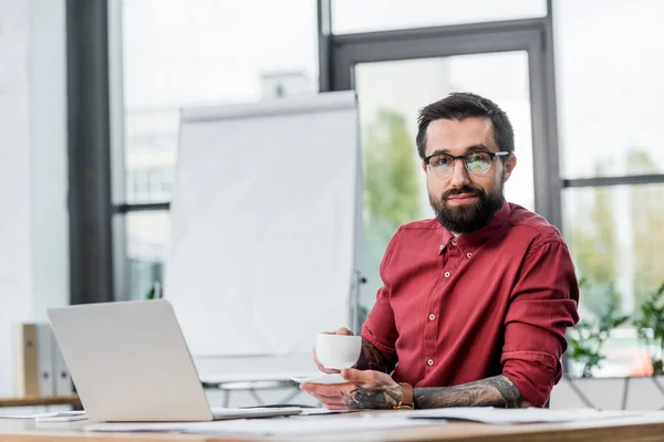 Sorrindo gerente de conta sentado à mesa e segurando xícara de café — Stock Photo