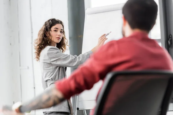 Selective focus of account manager pointing at flipchart and talking with colleague — Stock Photo