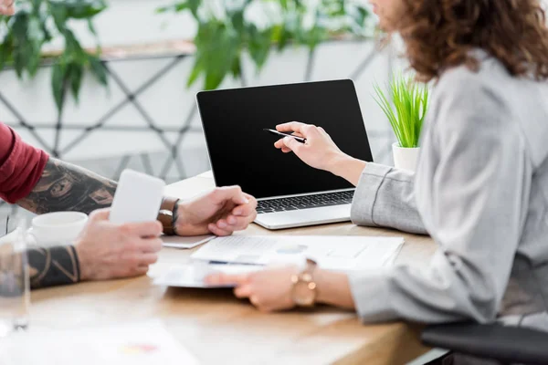 Vista ritagliata di account manager che punta con il dito al computer portatile e tenendo lo smartphone — Foto stock