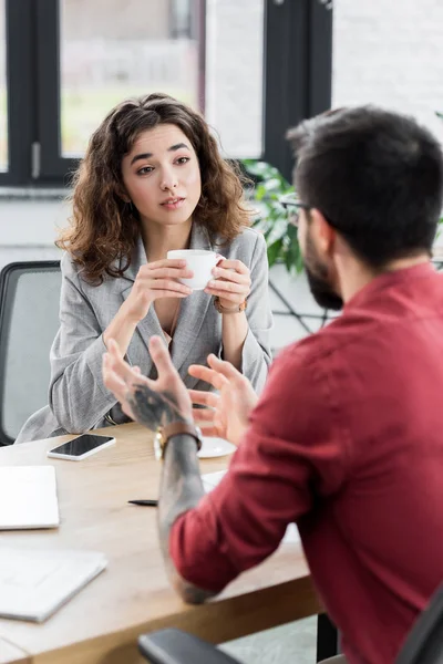 Selektiver Fokus des Kontoverwalters, der Tasse hält und dem Kollegen zuhört — Stockfoto