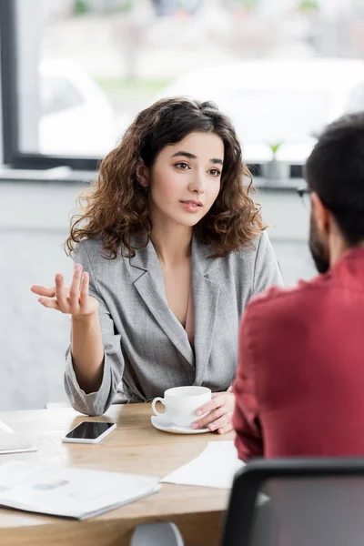 Messa a fuoco selettiva di account manager parlando con il collega e tenendo tazza — Foto stock