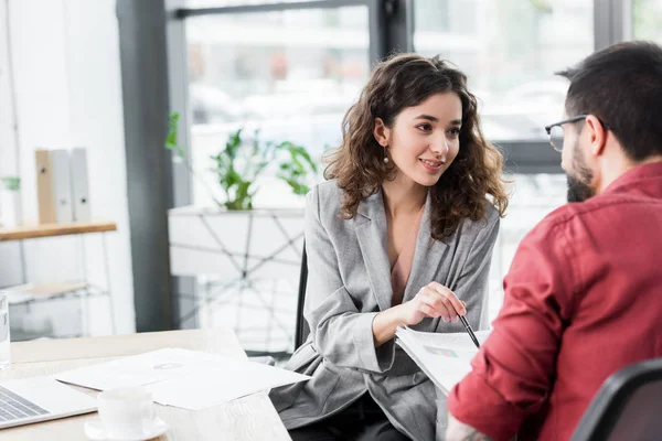 Selective focus of smiling account manager pointing at papers and talking with colleague — Stock Photo