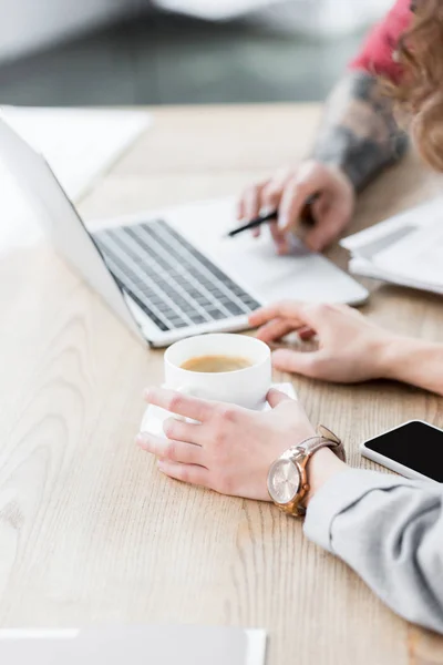 Cropped view of account managers sitting at table and holding cup — Stock Photo