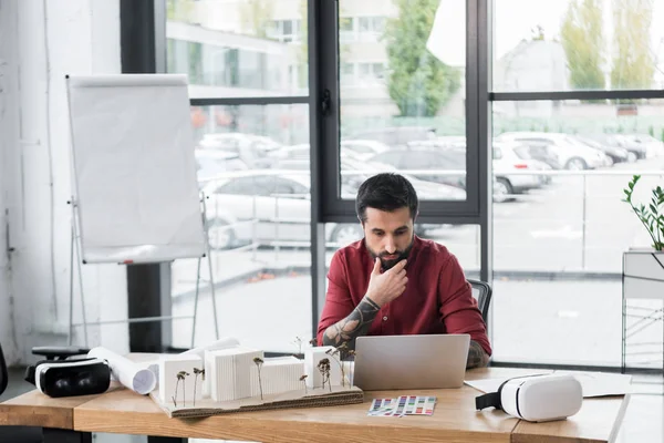 Pensive virtual reality architect using laptop and sitting at table — Stock Photo