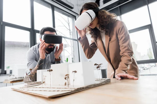 Virtual reality architects in virtual reality headsets looking at model of house — Stock Photo