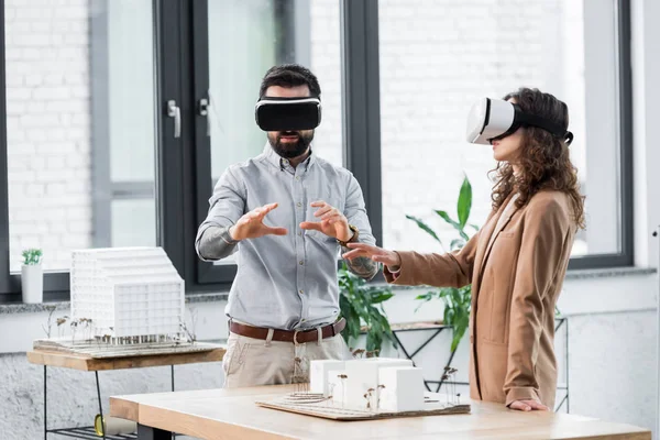 Arquitectos de realidad virtual en auriculares de realidad virtual gesticulando y mirando el modelo de casa - foto de stock