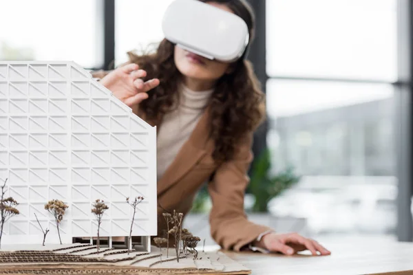 Selective focus of virtual reality architect in virtual reality headset looking at model of house — Stock Photo