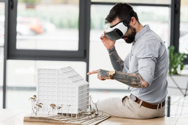 Архитектор виртуальной реальности в гарнитуре виртуальной реальности, указывающий пальцем на модель дома — стоковое фото