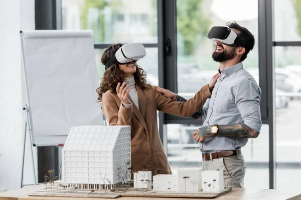 Улыбающиеся архитекторы виртуальной реальности в наушниках виртуальной реальности разговаривают в офисе — стоковое фото