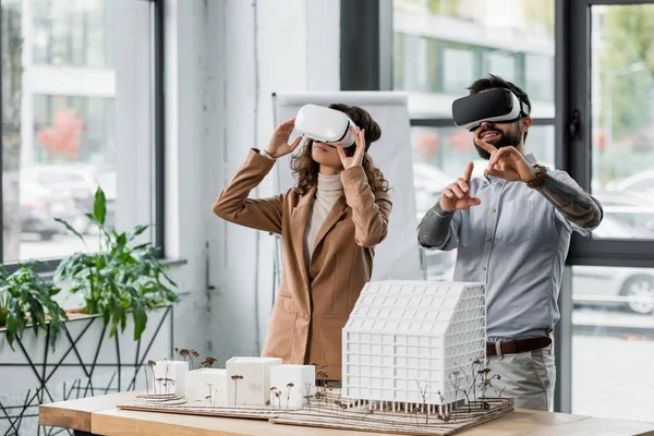 Arquitectos de realidad virtual sonrientes en auriculares de realidad virtual apuntando con el dedo - foto de stock
