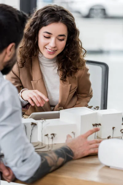 Enfoque selectivo de sonriente arquitecto de realidad virtual apuntando con el dedo al modelo de casa - foto de stock