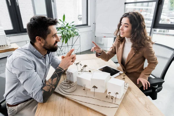 Sonrientes arquitectos de realidad virtual sentados a la mesa y hablando en la oficina - foto de stock