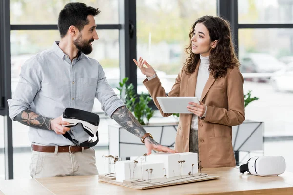 Smiling virtual reality architects talking and standing near model of house in office — Stock Photo